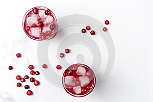 Cranberry cocktail in crystal glasses with ice decorated by berries on white bright marble background. Flat lay style