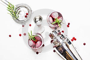 Cranberry cocktail with ice, rosemary and berries, bar tools, white background, top view