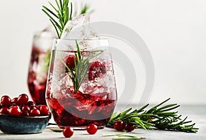 Cranberry cocktail or mocktail with ice, rosemary and red berries in tumbler glass, gray background, copy space