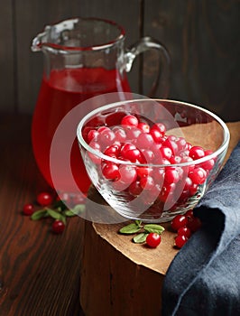 Cranberry cold drink in glass pitcher with red berries on wooden rustic background