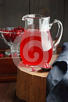 Cranberry cold drink in glass pitcher with red berries on wooden rustic background, closeup, winter christmas holiday drinks