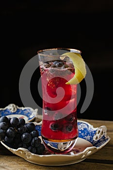 Cranberry color cocktail garnished with fresh grapes on a vinta