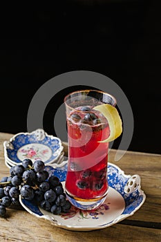 Cranberry color cocktail garnished with fresh grapes on a vinta