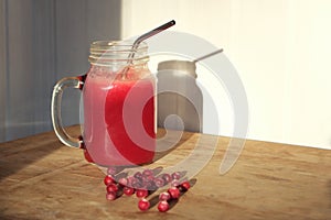 Cranberry juice in mason jar with fresh berries on wooden table with shadow on white wall. Homemade vitamin drink