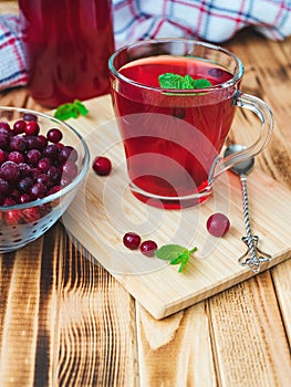 cranberry juice with mint leaves in a glass cup on a bamboo board with a teaspoon on a background of berries and a bottle