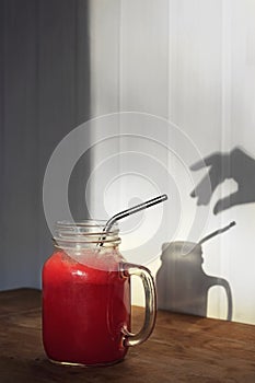 Cranberry juice or smoothie from fresh berries in mason jar on wooden table with shadow of woman hand on white wall. Homemade