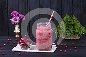 Cranberry juice smoothie shake in glass mug and raw cranberry on black wooden background, close up