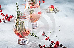 Cranberry, vodka and gin alcoholic cocktail with ice and thyme in special glass. Winter aperitif drink. Gray background. Christmas