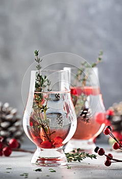 Cranberry, vodka and gin alcoholic cocktail with ice and thyme in special glass. Winter aperitif drink. Gray background. Christmas