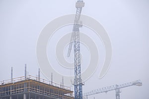 Crane on the background of under construction skyscrapers in a fog on an abandoned