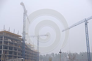 Crane on the background of under construction skyscrapers in a fog on an abandoned