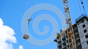 Crane and building construction site against blue sky. heavy load hanging on the hook of a crane on the construction of