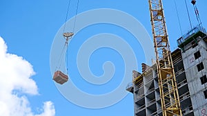 Crane and building construction site against blue sky. heavy load hanging on the hook of a crane on the construction of