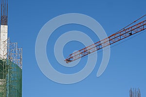 Crane and building construction site against blue sky. Metal construction of unfinished building on construction. Tower