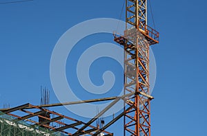 Crane and building construction site against blue sky. Metal construction of unfinished building on construction. Tower