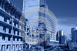 Crane and building construction site against blue sky, toned trendy classic blue color of year 2020