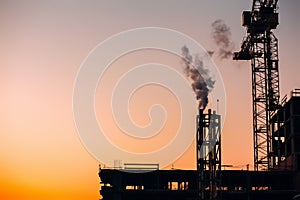 Crane and building construction site with pipe with smoke on background of sunset sky. Industrial landscape with silhouettes of c