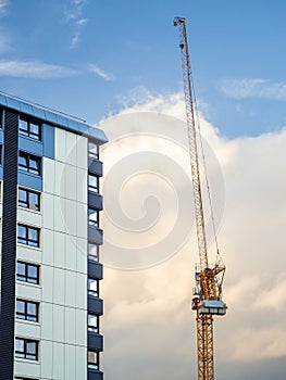 Crane at a construction site of an apartment building set against a blue cloudy sky