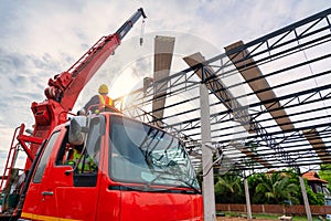 A crane driver is steering a crane to lift a roof or PU foam roof sheet onto a steel roof structure at a construction site.