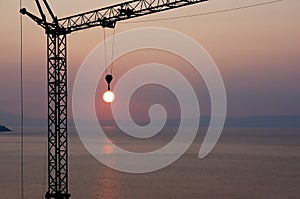 Crane hook catching sun during sunset over the sea