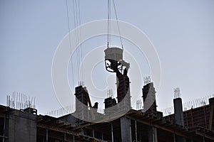 Crane lifting a concrete bucket on sunset background. Silhouettes of builders pouring cement mix for formworks at a construction