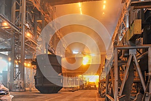 Crane lifting up filled metal container scrap in the burning ladle furnace with hot steel inside. Metallurgical factory