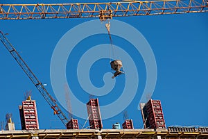 A crane lifts concrete for a modern metal-concrete structure of a residential building. Container with concrete against the blue