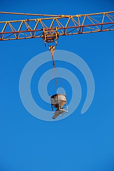 A crane lifts concrete for a modern metal-concrete structure of a residential building. Container with concrete against the blue
