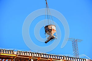 A crane lifts concrete for a modern metal-concrete structure of a residential building. Container with concrete against the blue