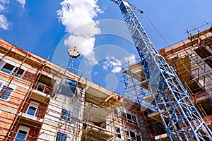 Crane lifts wheelbarrow full of mortar, in background is edifice under construction, building site