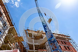 Crane lifts wheelbarrow full of red bricks, in background is edifice under construction, building site