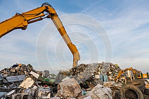 A crane moves pieces of metal through mountains of scrap metal in a scrap yard