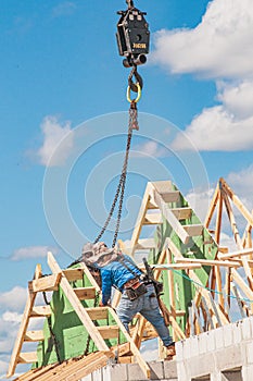Crane moving roof trusses, into place and two men are securing the truss