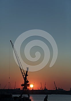 Crane on a pier silhouetted against the sunset in the harbor