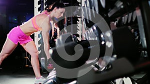Crane shot: Athletic woman starts training. Trains back muscles with dumbbells in the spotlight