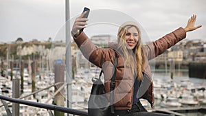 Crane shot. Happy young attractive stylish girl young woman blogger in port do a selfie at her cell phone and scream