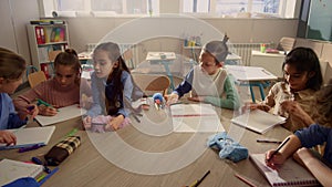 Students talking during lesson at round desk. Cheerful kids having lesson