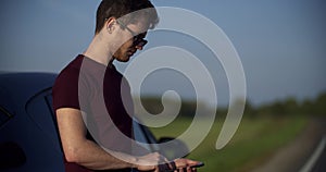 Crane shot of portrait of young man looks at something in the phone, a broken car on the road in the frame on the