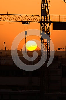 Crane silhouette over sun under construction