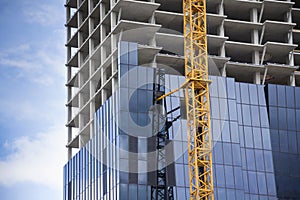 Crane on skyscraper construction site with windows reflecting sky