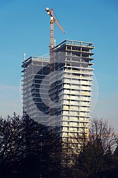 Crane on skyscraper construction site with windows reflecting sky