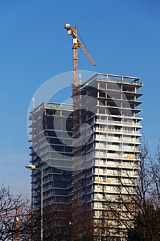 Crane on skyscraper construction site with windows reflecting sky