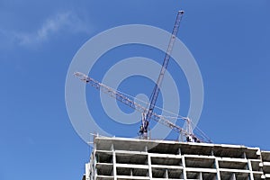 Crane working on a building under construction in day time.