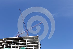 Crane working on a building under construction in day time.