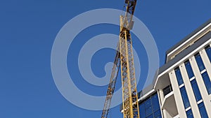 Crane working on construction site under blue sky. Construction of a modern glass building