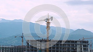 Cranes builds multistorey house on construction site in the city with mountains on background at sunset . Industry of
