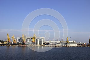 Cranes and granaries, cisterns with wheat in the port in clear weather, the sea