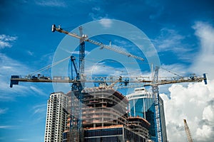 Cranes on modern skyscraper construction in city at sunny day with blue sky