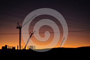 Cranes, Power Lines and Industrial Factories Silhouetted Against the Sunset