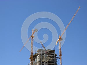 Cranes and under-construction apartment building against blue sky.